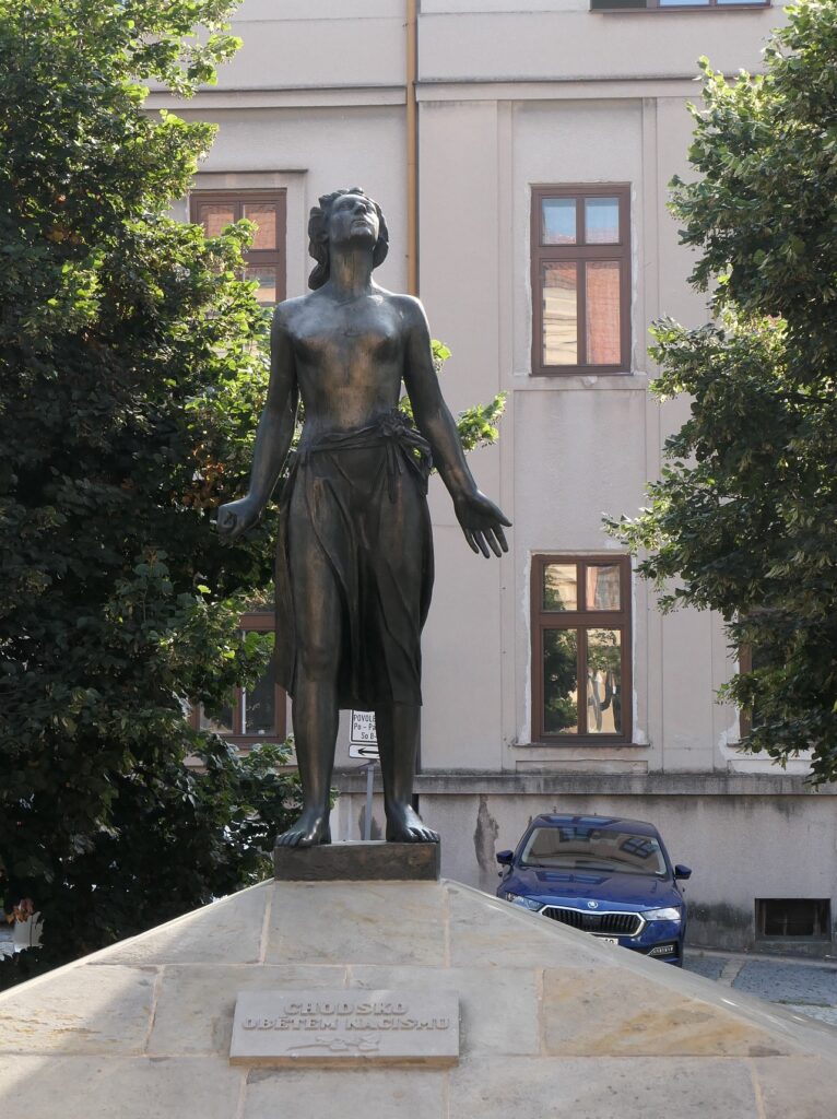 Domažlice, Pomník obětem nacismu z roku 1948 od sochaře Otakara Švece (1892–1955). Původně měl být dedikován Zdeňkovi Bořkovi Dohalskému (1900–1945), novináři a odbojáři z Domažlicka se šlechtickými kořeny a prominentními vazbami na prvorepublikovou, protektorátní a exilovou vládu popravenému v únoru 1945 v Terezíně. Po únoru 1948 se ale vzpomínka na jeho osobu stala nežádoucí a jeho jméno nechali místní funkcionáři z dedikace chodským obětem nacismu zcela odstranit /foto autorů