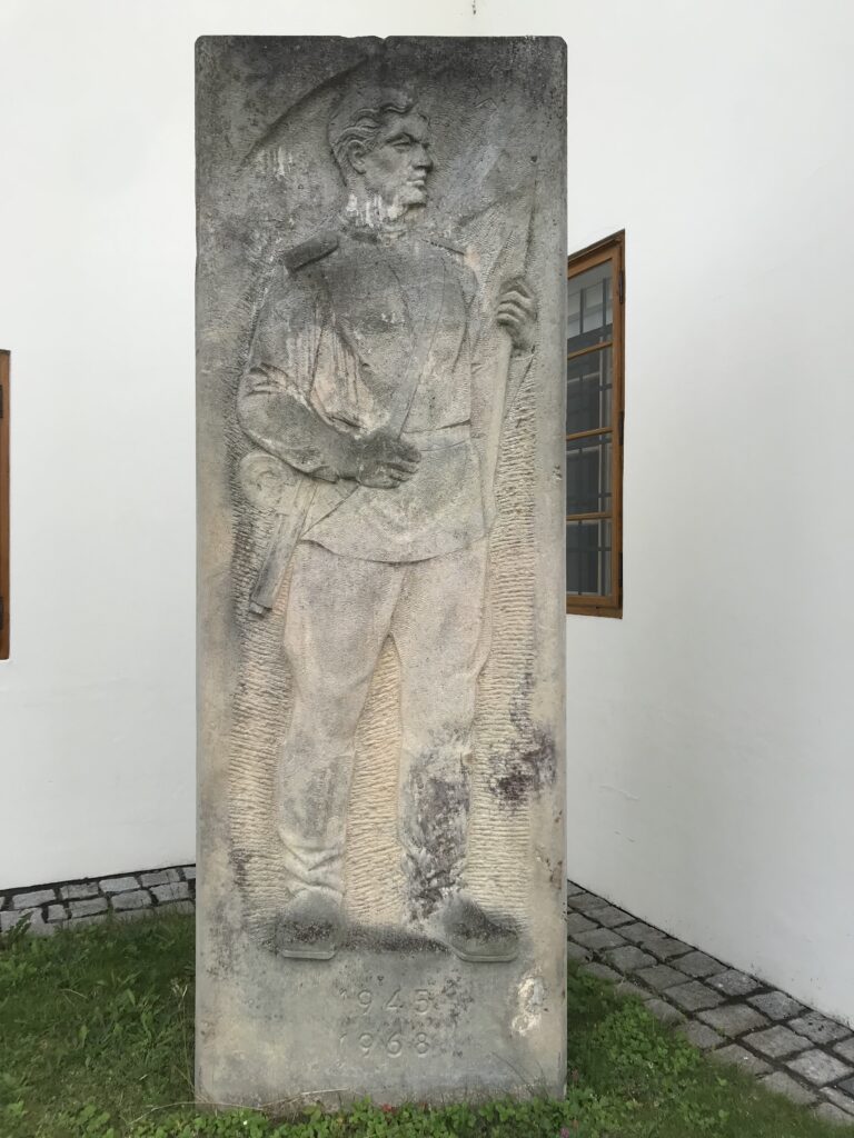 Ústřední reliéf s postavou rudoarmějce a letopočty 1945 a 1968 u nohou; depozitář Muzea Jindřichohradecka /foto autorů