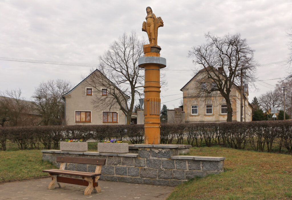 Památník osvobození v Pernarci (osvobozeném Američany) od Aloise Sopra (1913–1993) se sochou družstevnice alegorizující úrodu socialistického venkova a nápisem Čest a sláva slavné Rudé armádě (1975) /foto Pavel Hrdlička, Wikimedia Commons, File:Pernarec, common, statue.jpg