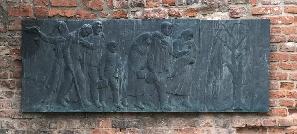 Deskový reliéf Břetislava Bendy (1897–1983), o jehož instalaci v Praze-Holešovicích protifašističtí bojovníci od roku 1970 marně usilovali. Nakonec byl zástupně a v neúplné podobě odhalen v červnu 1988 v Terezíně, bez nepoužitelné desky původního triptychu s nápisem Z těchto míst bývalého Radiotrhu odvlekli nacisté v letech 1941–1945 do koncentračních a vyhlazovacích táborů celkem 45 413 mužů, žen a dětí, z nichž se 37 669 nevrátilo. /foto autorů